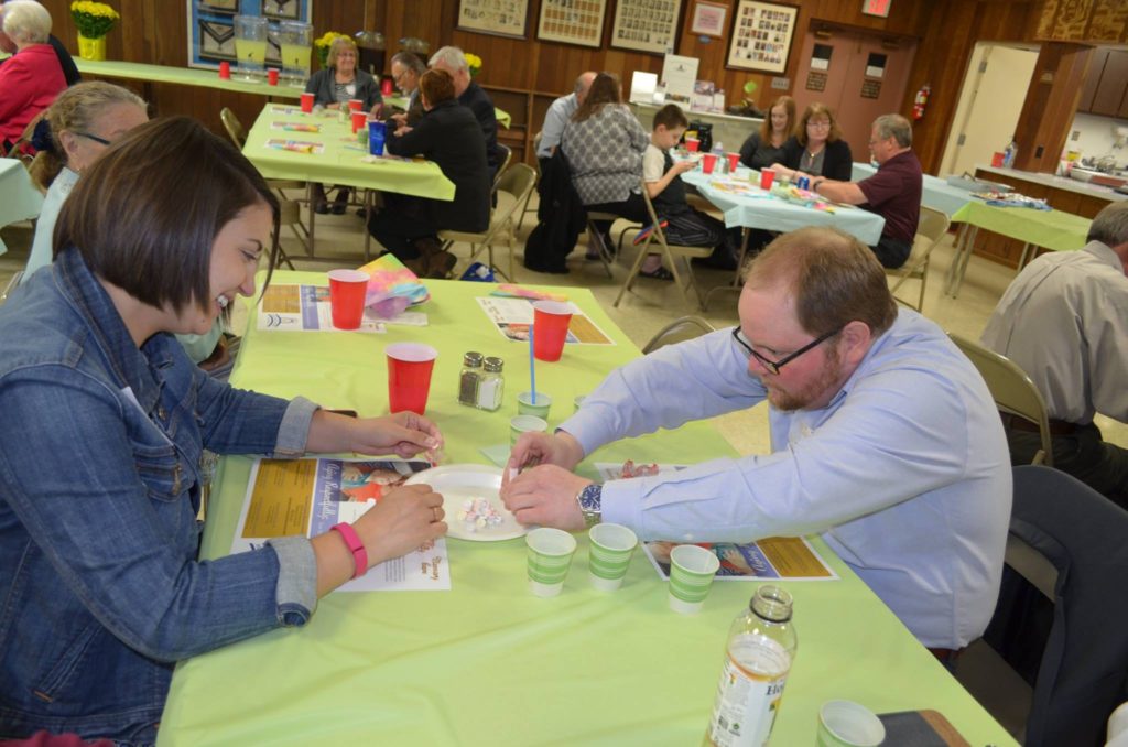 Young couple seated at table compete against others in Smarties Stacking Challenge at a recent Ladies Night Dinner at J.B. Covert Lodge