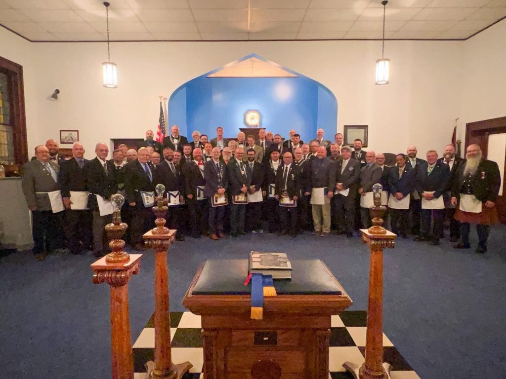 A group of Freemasons standing together inside a Masonic lodge room at East Palestine Lodge No. 417 during a stated meeting, with the lodge altar and furnishings visible in the foreground.