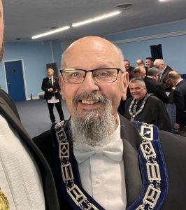 A man wearing glasses and formal Masonic regalia smiles for a photo.
