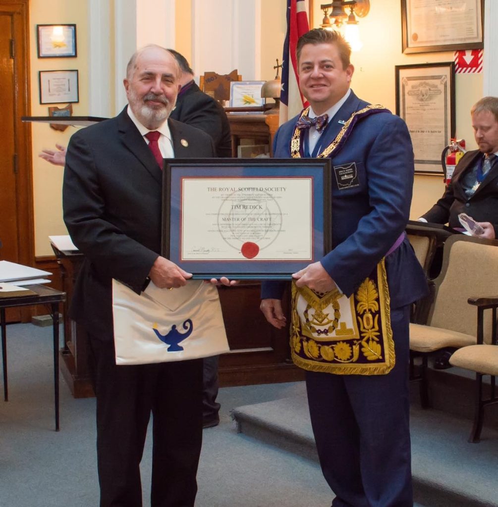 Two men stand side by side holding a large frame, both dressed in traditional Masonic regalia